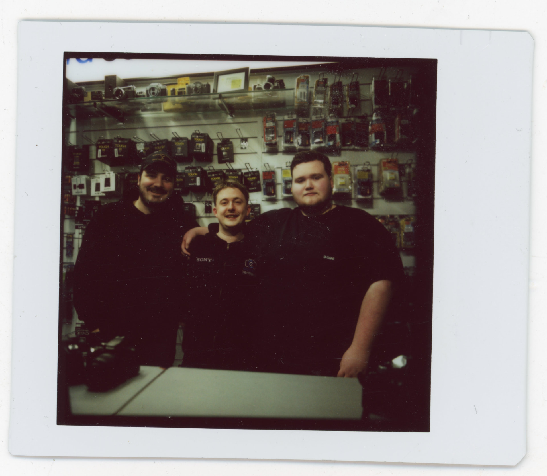 Instax photo of three Camera Centre UK staff members behind the counter